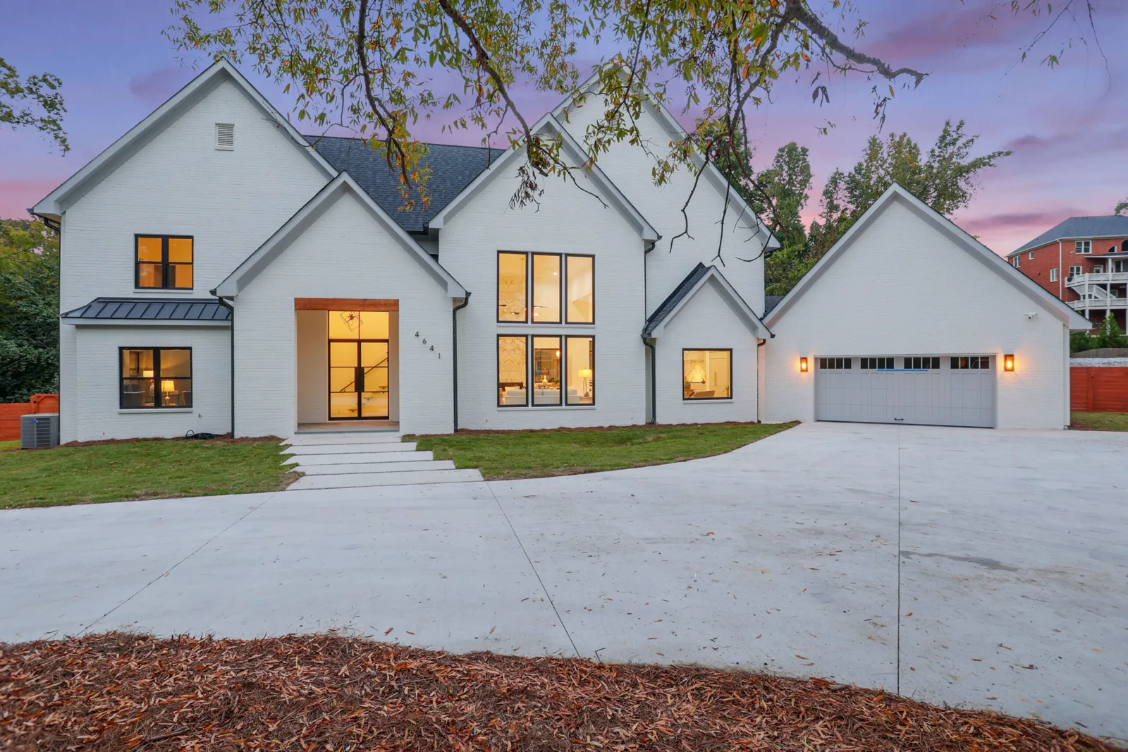 Completed custom home by Armogan Construction Group at 4641 Woodland Brook Drive SE: a white modern-farmhouse residence with black-framed windows, photographed at dusk.