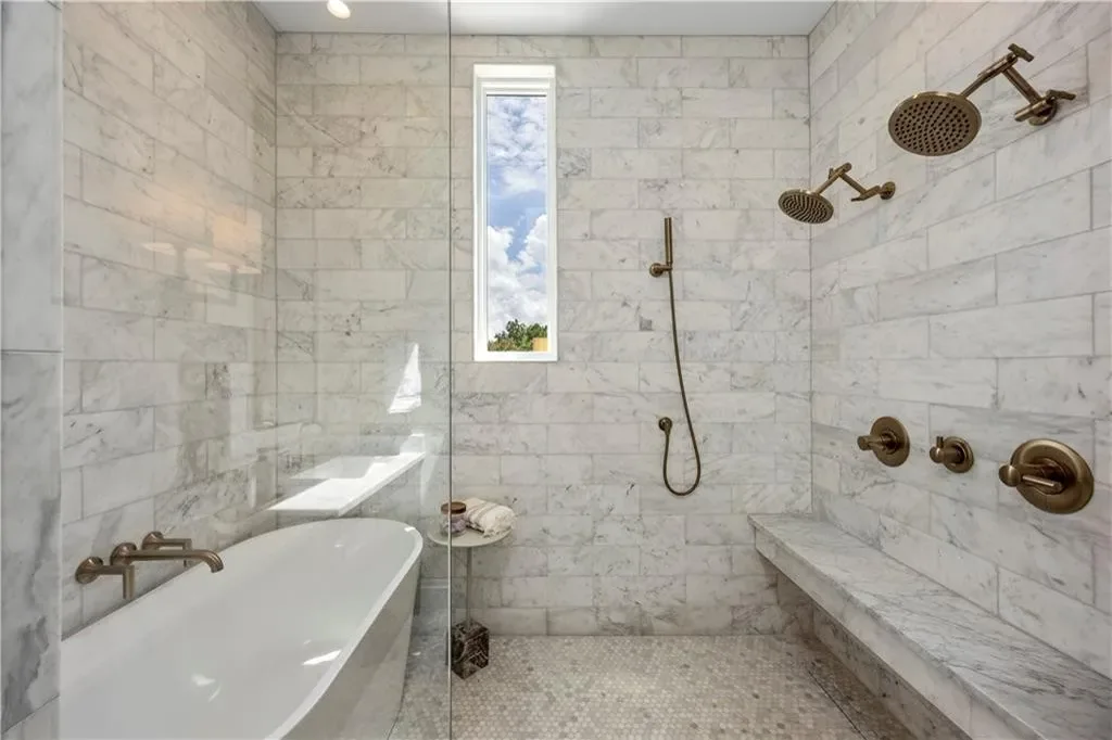 Primary bath of the model townhome: marble wet room with a freestanding tub, brass fixtures, and a marble bench.