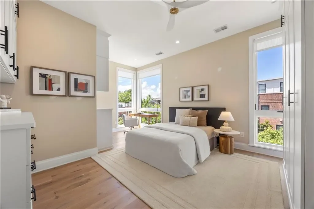 Bedroom of the model townhome with tall corner windows, warm neutral palette, and a small work desk by the glass.