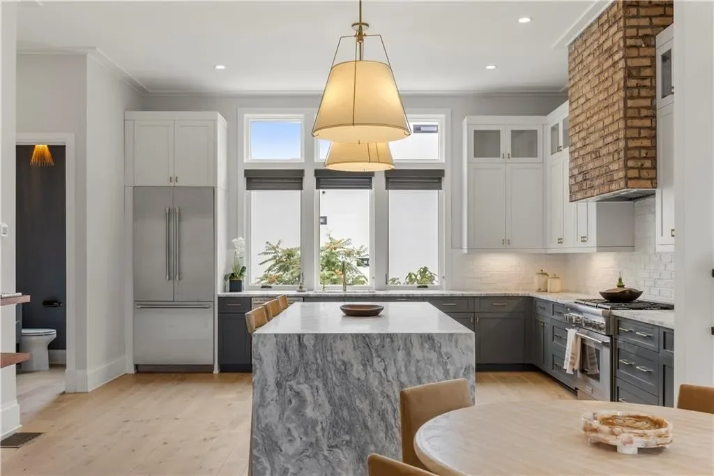 Kitchen of the model townhome with a marble waterfall island, brick range hood, and professional appliances.