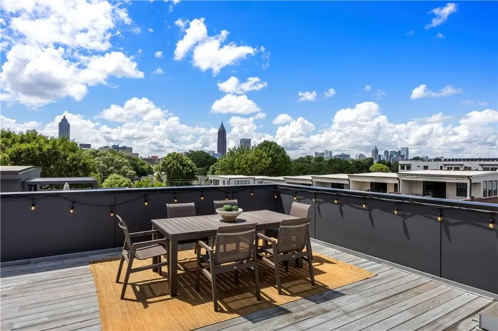 Rooftop terrace of the model townhome on a bright day: outdoor dining table under string lights with the Midtown Atlanta skyline on the horizon.